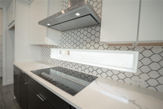 kitchen with light stone countertops, range hood, white cabinets, black electric cooktop, and dark cabinets