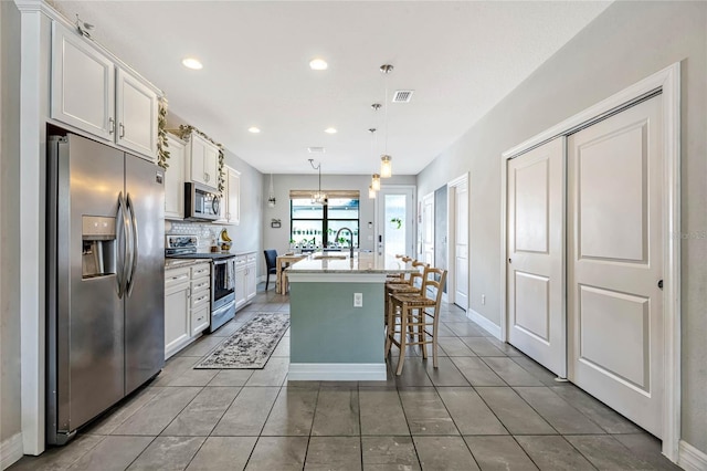 kitchen featuring white cabinetry, stainless steel appliances, a kitchen island with sink, and pendant lighting