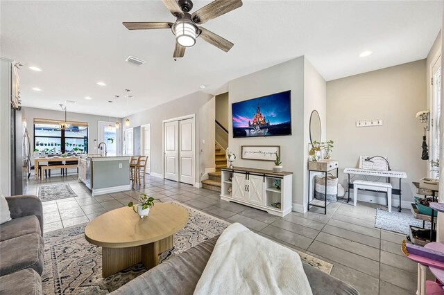 living area featuring visible vents, dark tile patterned flooring, ceiling fan with notable chandelier, baseboards, and stairs