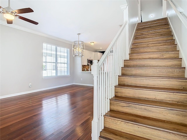 staircase featuring hardwood / wood-style flooring, crown molding, and ceiling fan with notable chandelier