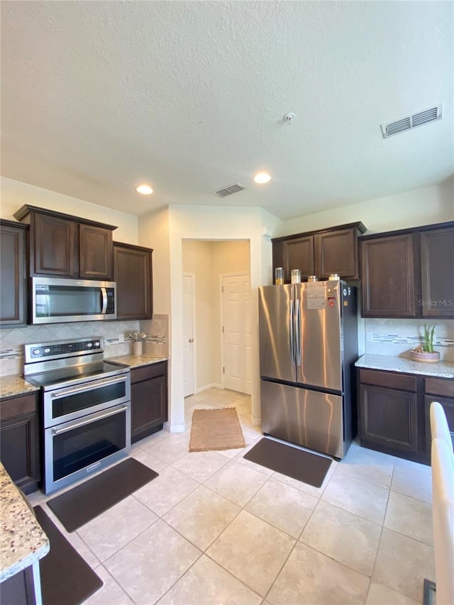 kitchen with tasteful backsplash, light tile patterned floors, dark brown cabinets, and stainless steel appliances