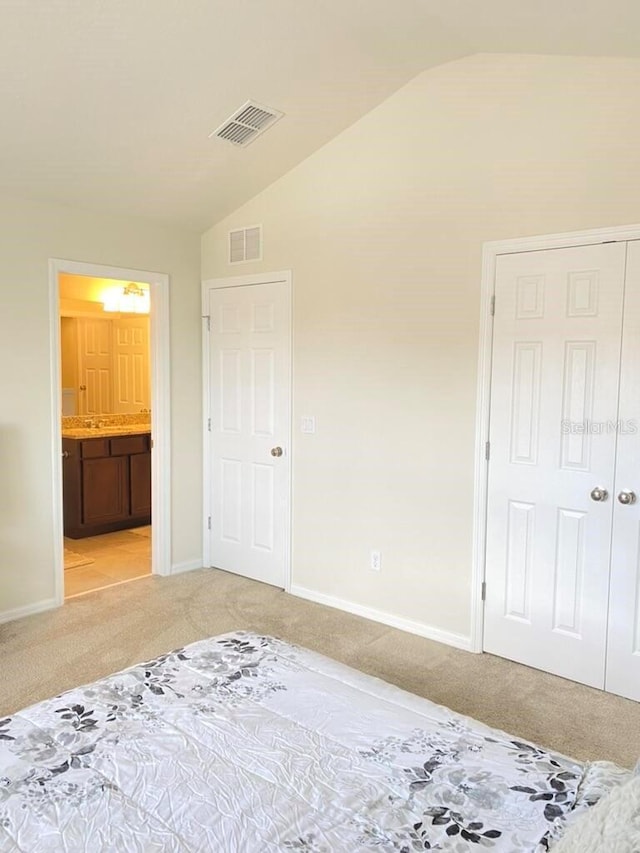 bedroom featuring ensuite bathroom, lofted ceiling, light colored carpet, and a closet