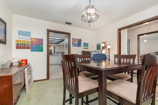 dining space featuring light carpet, a notable chandelier, and a textured ceiling