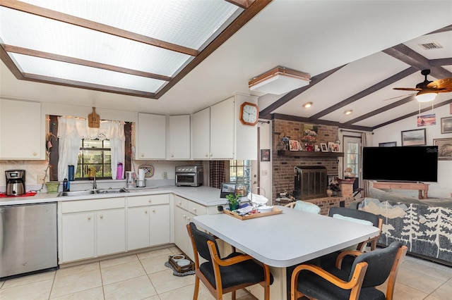 kitchen featuring sink, white cabinetry, lofted ceiling with beams, a brick fireplace, and dishwasher