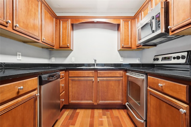 kitchen with sink, light wood-type flooring, dark stone counters, and appliances with stainless steel finishes