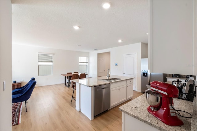 kitchen with white cabinetry, sink, a kitchen island with sink, stainless steel dishwasher, and light hardwood / wood-style flooring