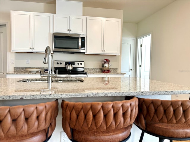 kitchen featuring white cabinets, a kitchen bar, stainless steel appliances, and light stone countertops