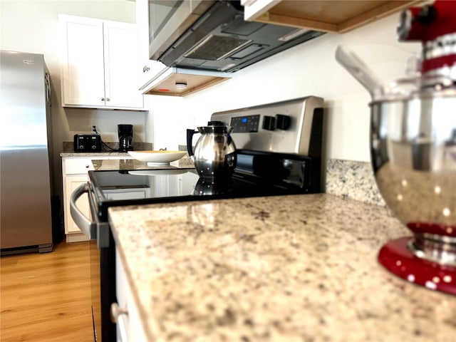 kitchen with exhaust hood, stainless steel appliances, light stone countertops, light hardwood / wood-style floors, and white cabinetry