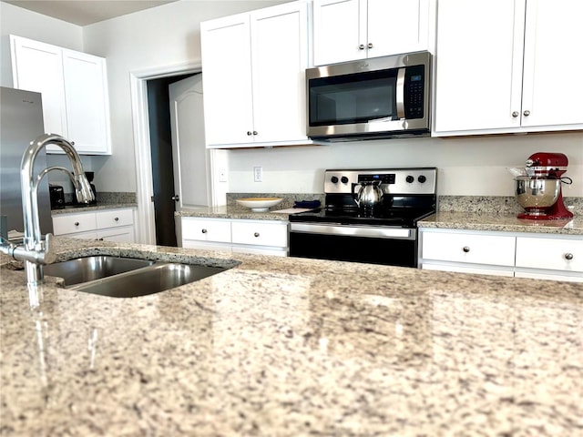 kitchen featuring white cabinetry, stainless steel appliances, light stone counters, and sink