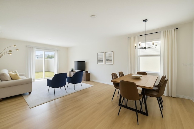 dining room with light wood-style flooring, a notable chandelier, and baseboards