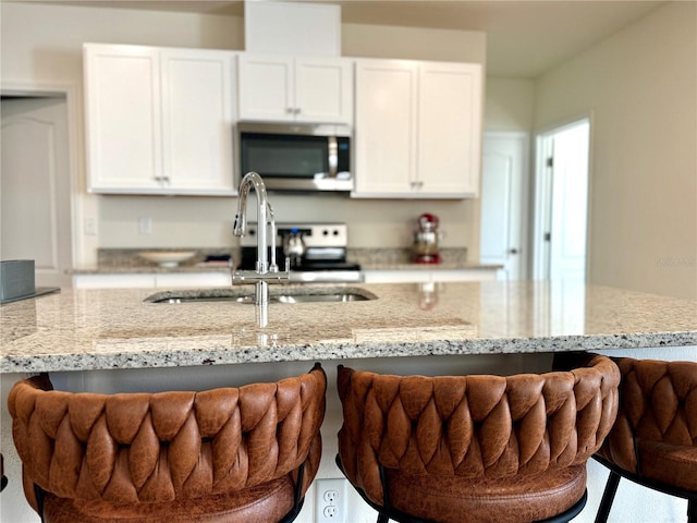 kitchen with white cabinetry, stainless steel microwave, a breakfast bar, a sink, and light stone counters