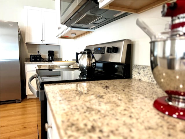kitchen with white cabinetry, light stone counters, light wood finished floors, range with electric stovetop, and freestanding refrigerator