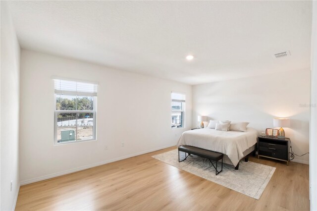 bedroom featuring multiple windows, visible vents, light wood-style floors, and baseboards
