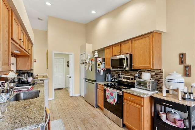 kitchen with light stone counters, sink, backsplash, and stainless steel appliances