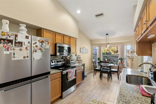 kitchen featuring sink, hanging light fixtures, stainless steel appliances, light stone countertops, and light hardwood / wood-style flooring