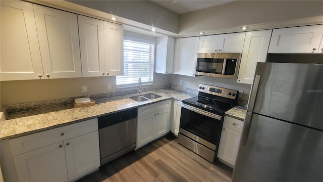 kitchen with sink, appliances with stainless steel finishes, white cabinetry, light stone countertops, and light wood-type flooring