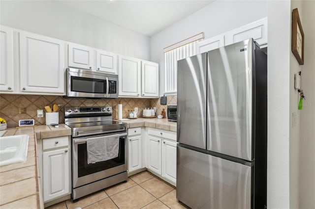 kitchen with light tile patterned flooring, tile countertops, appliances with stainless steel finishes, white cabinets, and backsplash