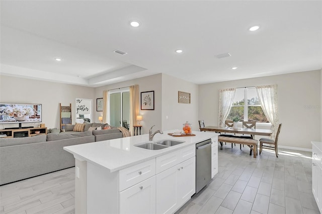 kitchen with sink, white cabinets, a kitchen island with sink, stainless steel dishwasher, and a tray ceiling