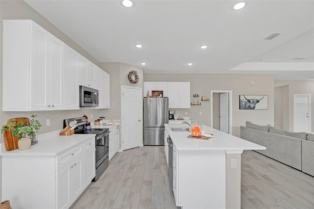 kitchen with appliances with stainless steel finishes, white cabinetry, sink, light hardwood / wood-style floors, and a center island with sink