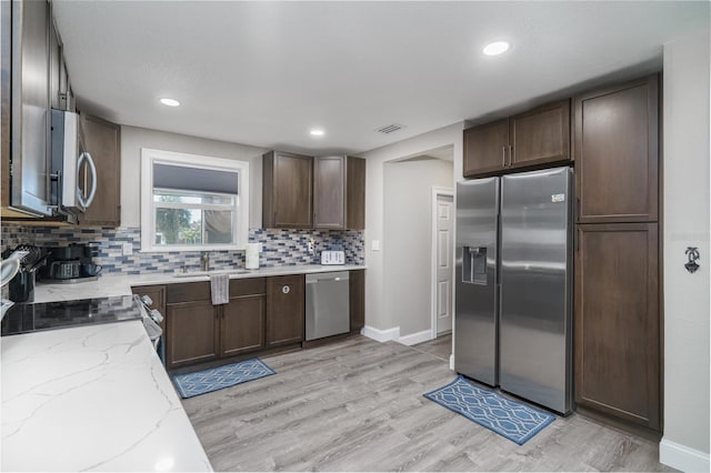 kitchen featuring sink, stainless steel appliances, light stone countertops, decorative backsplash, and light wood-type flooring