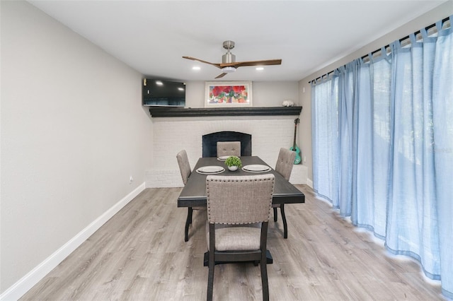 dining area featuring ceiling fan, light hardwood / wood-style floors, and a brick fireplace