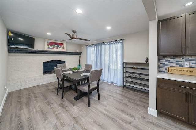 dining area with a fireplace, light hardwood / wood-style floors, and ceiling fan