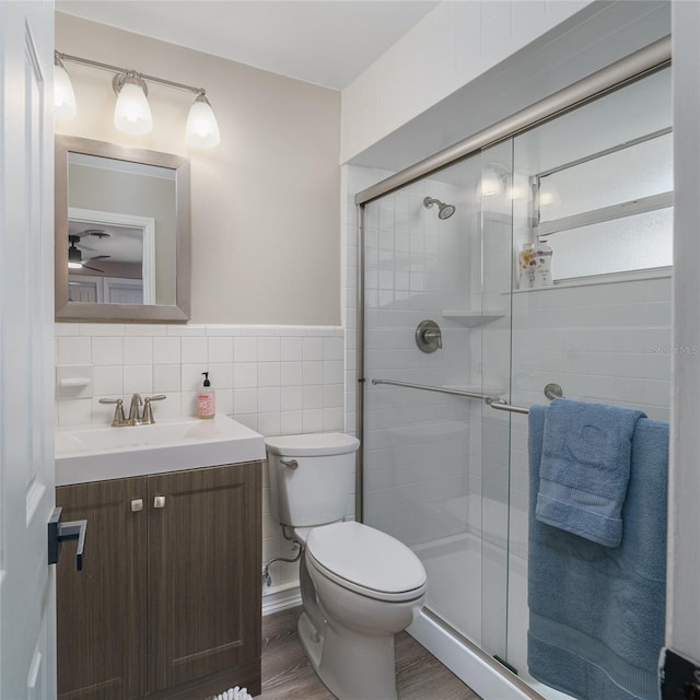 bathroom featuring vanity, toilet, a shower with door, and tile walls