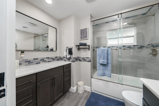 full bathroom with hardwood / wood-style flooring, shower / bath combination with glass door, vanity, a textured ceiling, and toilet