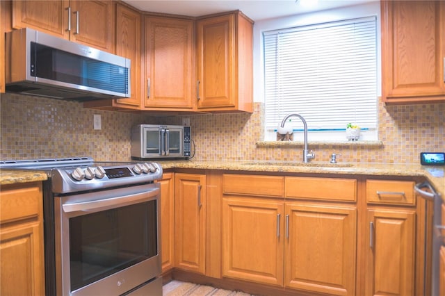 kitchen featuring light stone counters, sink, decorative backsplash, and stainless steel appliances