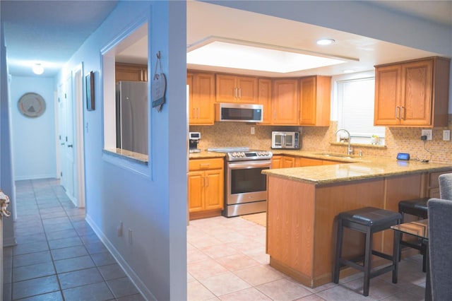 kitchen featuring a breakfast bar, sink, appliances with stainless steel finishes, kitchen peninsula, and decorative backsplash