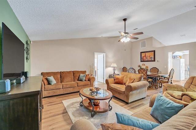 living room featuring lofted ceiling, ceiling fan, light hardwood / wood-style floors, and a textured ceiling