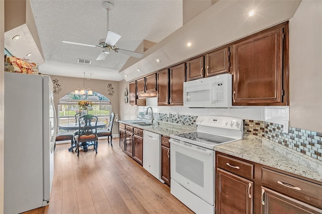 kitchen featuring sink, decorative light fixtures, vaulted ceiling, light wood-type flooring, and white appliances