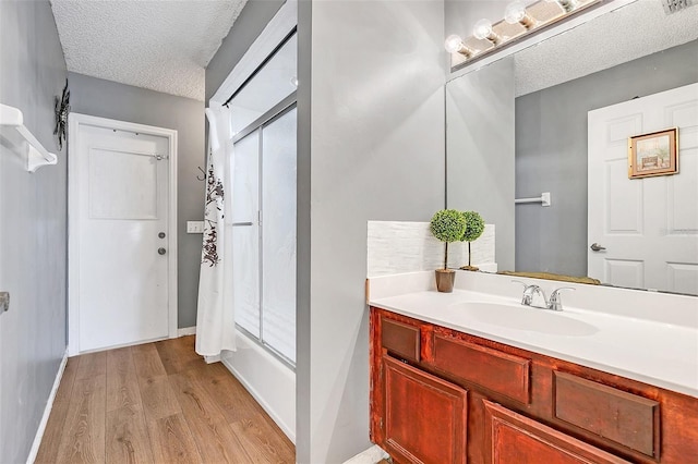 bathroom with vanity, bath / shower combo with glass door, wood-type flooring, and a textured ceiling