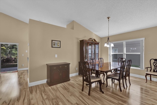 dining area with vaulted ceiling, a textured ceiling, a notable chandelier, and light hardwood / wood-style floors