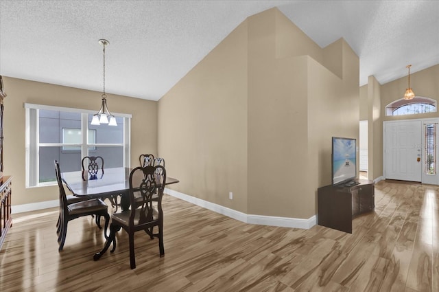 dining room with lofted ceiling, light hardwood / wood-style floors, a textured ceiling, and a notable chandelier