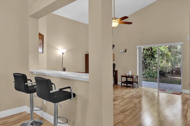 bar with ceiling fan, light hardwood / wood-style floors, and a high ceiling