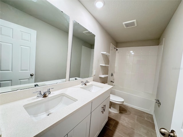 full bathroom with tiled shower / bath, vanity, toilet, and a textured ceiling