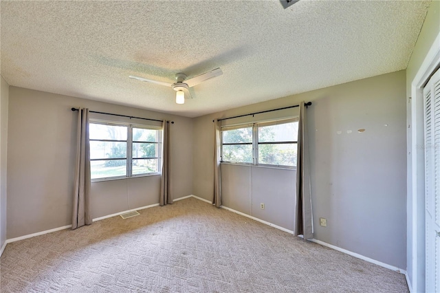 unfurnished bedroom featuring multiple windows, a textured ceiling, light colored carpet, and ceiling fan