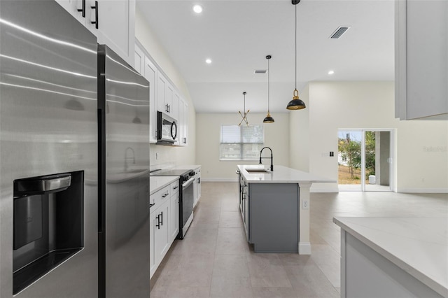 kitchen featuring appliances with stainless steel finishes, white cabinetry, an island with sink, hanging light fixtures, and light stone counters