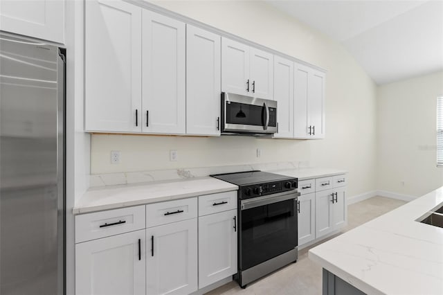 kitchen with light stone countertops, vaulted ceiling, stainless steel appliances, and white cabinets