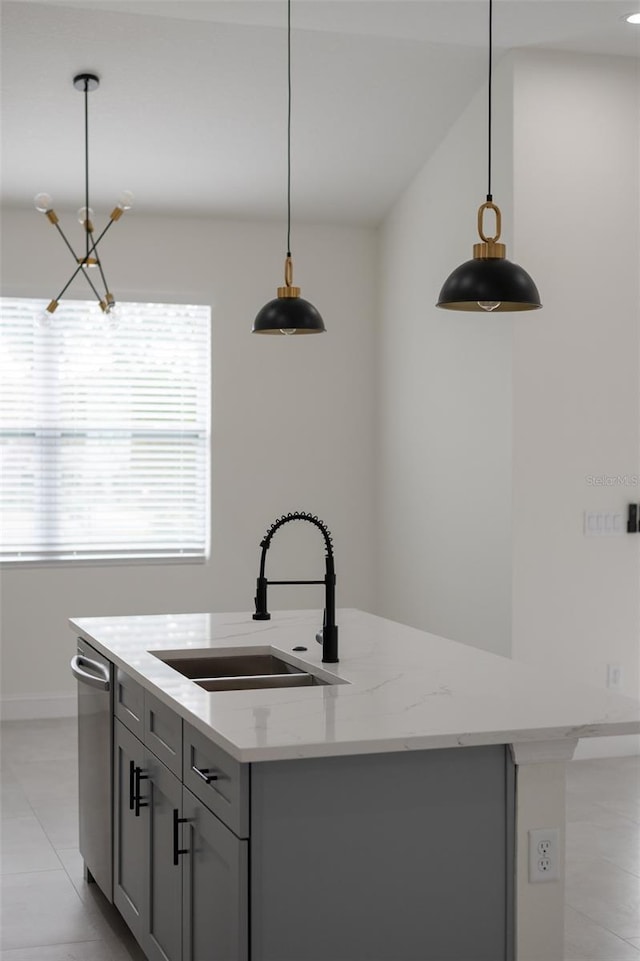 kitchen with decorative light fixtures, light stone countertops, sink, and a center island with sink