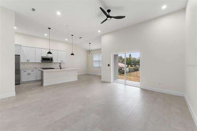 unfurnished living room with high vaulted ceiling, sink, and ceiling fan with notable chandelier