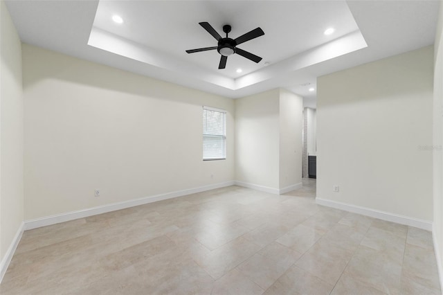 empty room with ceiling fan and a tray ceiling