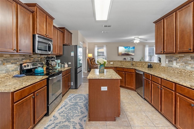 kitchen featuring sink, light tile patterned floors, appliances with stainless steel finishes, light stone counters, and a kitchen island