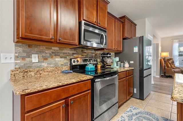 kitchen featuring light stone counters, stainless steel appliances, light tile patterned floors, and backsplash