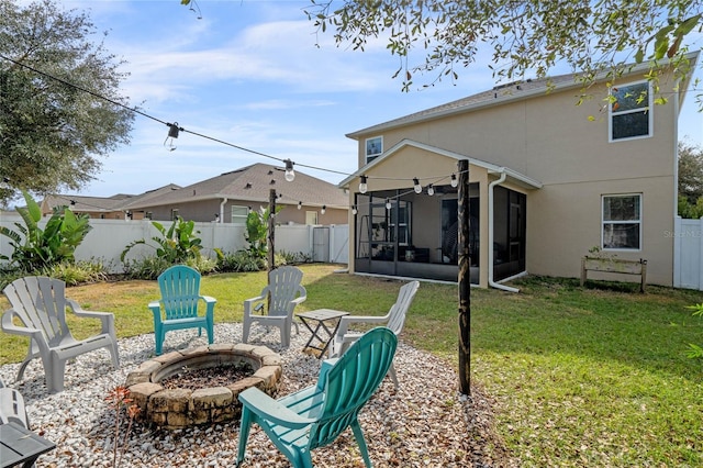 rear view of house with a sunroom, a yard, and a fire pit