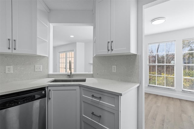 kitchen with sink, light hardwood / wood-style flooring, dishwasher, backsplash, and light stone countertops