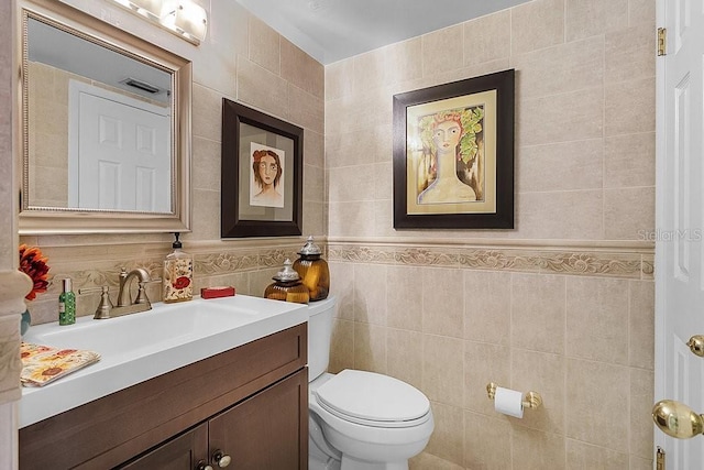 bathroom with vanity, toilet, and tile walls