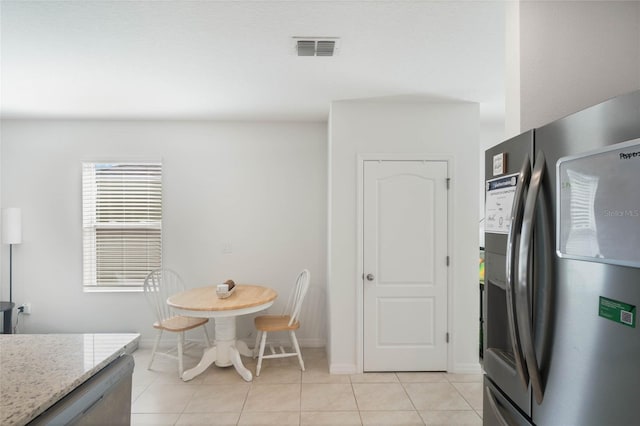 kitchen with light stone countertops, stainless steel refrigerator, and light tile patterned flooring