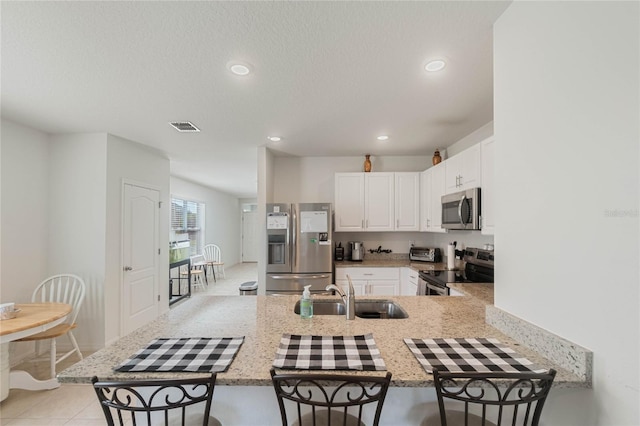 kitchen with appliances with stainless steel finishes, white cabinetry, sink, kitchen peninsula, and light stone countertops